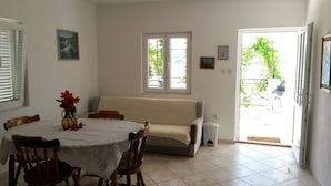A dining area with a round table, chairs, a sofa, and a window. - Apartments Janja (Solta)