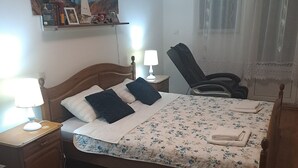 Un dormitorio ordenado con una cama de madera, una mesita de noche con una lámpara, una silla, una alfombra azul y un cuadro en la pared.