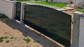 Un área cercada con césped, una montaña al fondo y un edificio con balcón.
