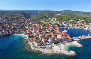 An aerial view of a coastal town with a marina, clear blue waters, and a hilly backdrop. - Apartments Pavao (Postira)