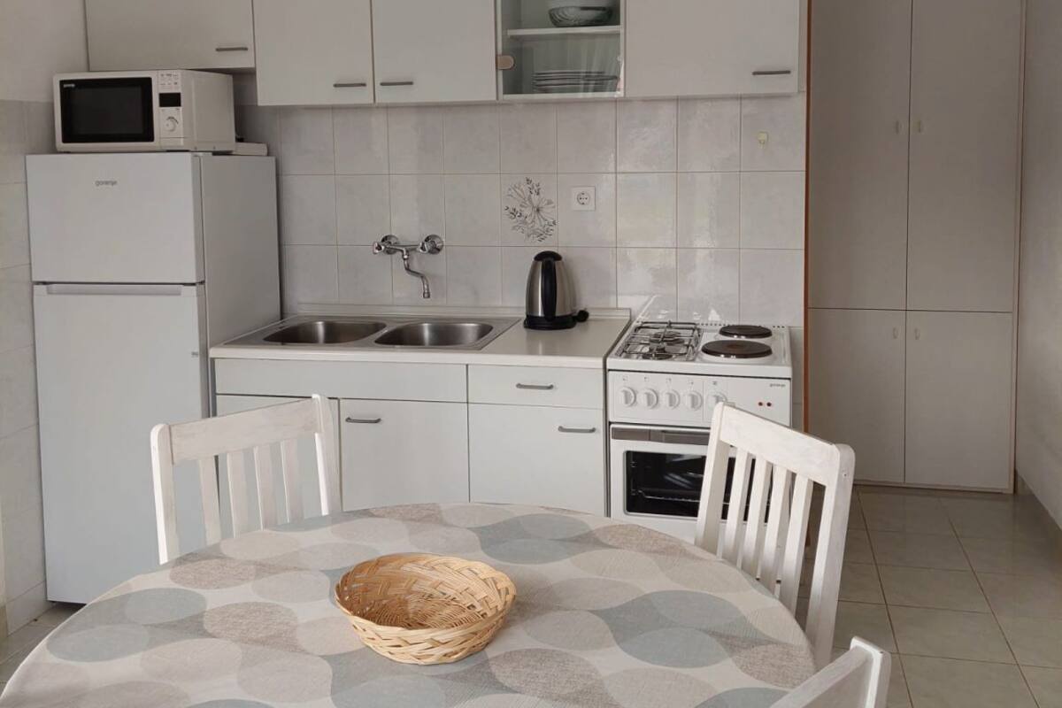 A compact kitchen with white cabinets, a microwave, a kettle, and a gas stove.