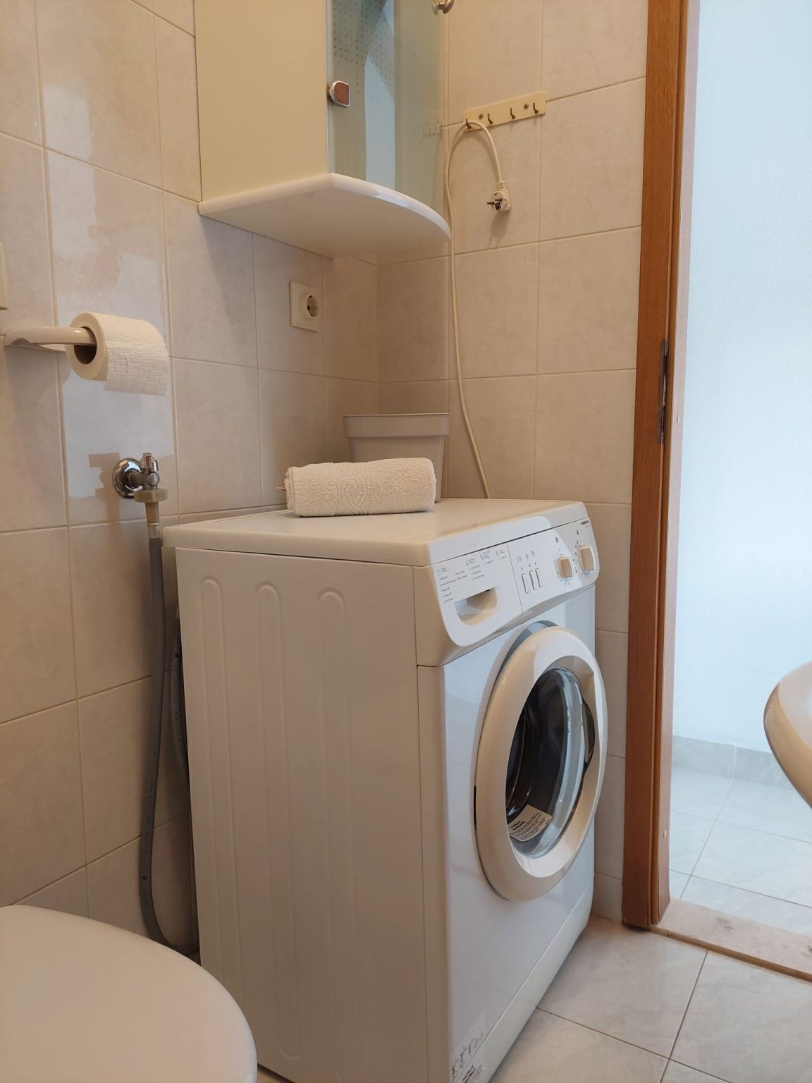 A compact, modern bathroom with a built-in washing machine, a toilet, and a shower area.