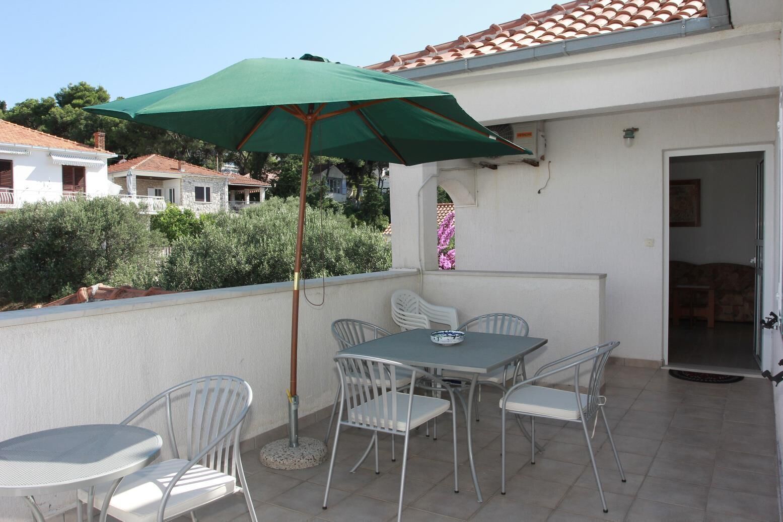 An outdoor patio with a table and chairs, a green umbrella, and a view of neighboring houses.