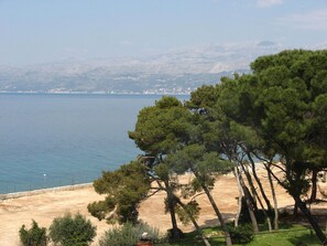 A coastal landscape with a sandy beach, dense pine trees, and a view of the sea and distant mountains. - Apartment Vinko (Postira)