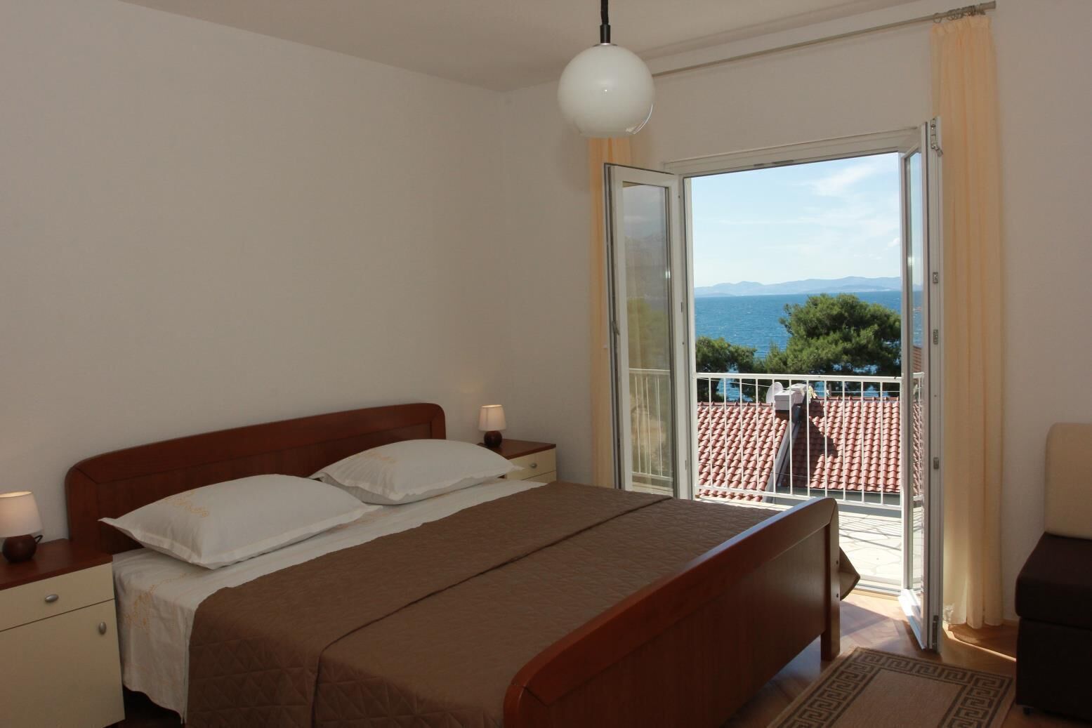 Une chambre à coucher avec un lit, des tables de chevet et une vue sur un balcon doté d’un toit en tuiles.