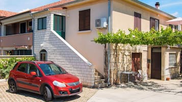 Ein rotes Auto vor einem Haus mit einem Ziegeldach, einer Steinfassade und einem kleinen Garten.