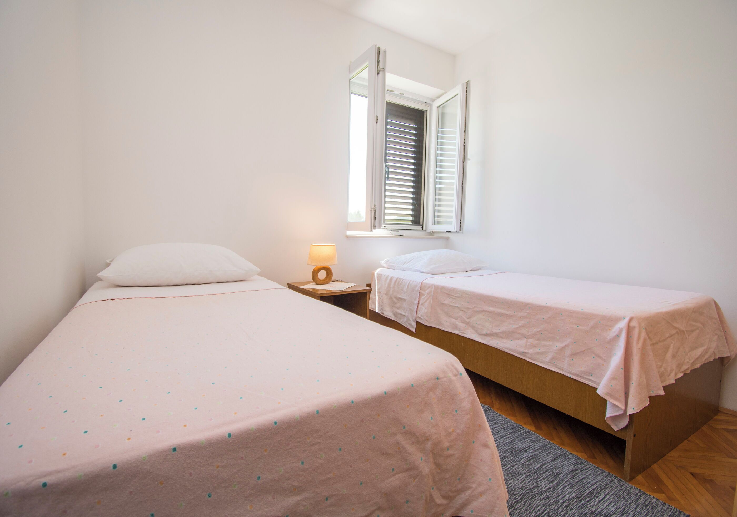 Een kleine, schone kamer met twee eenpersoonsbedden, een nachtkastje met lamp en een raam met jaloezieën.