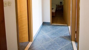 Un corridoio stretto con pavimento in piastrelle blu e porte in legno che conducono a una camera da letto.