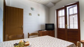 Un'area pranzo con un tavolo apparecchiato per due persone, un televisore su un mobile in legno e una porta con persiane di legno.