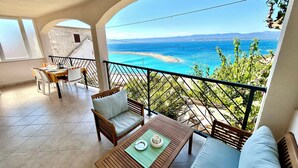 A balcony with a view of the sea, a dining area with chairs and a table, and a small garden area. - Apartments Matea (Bol)