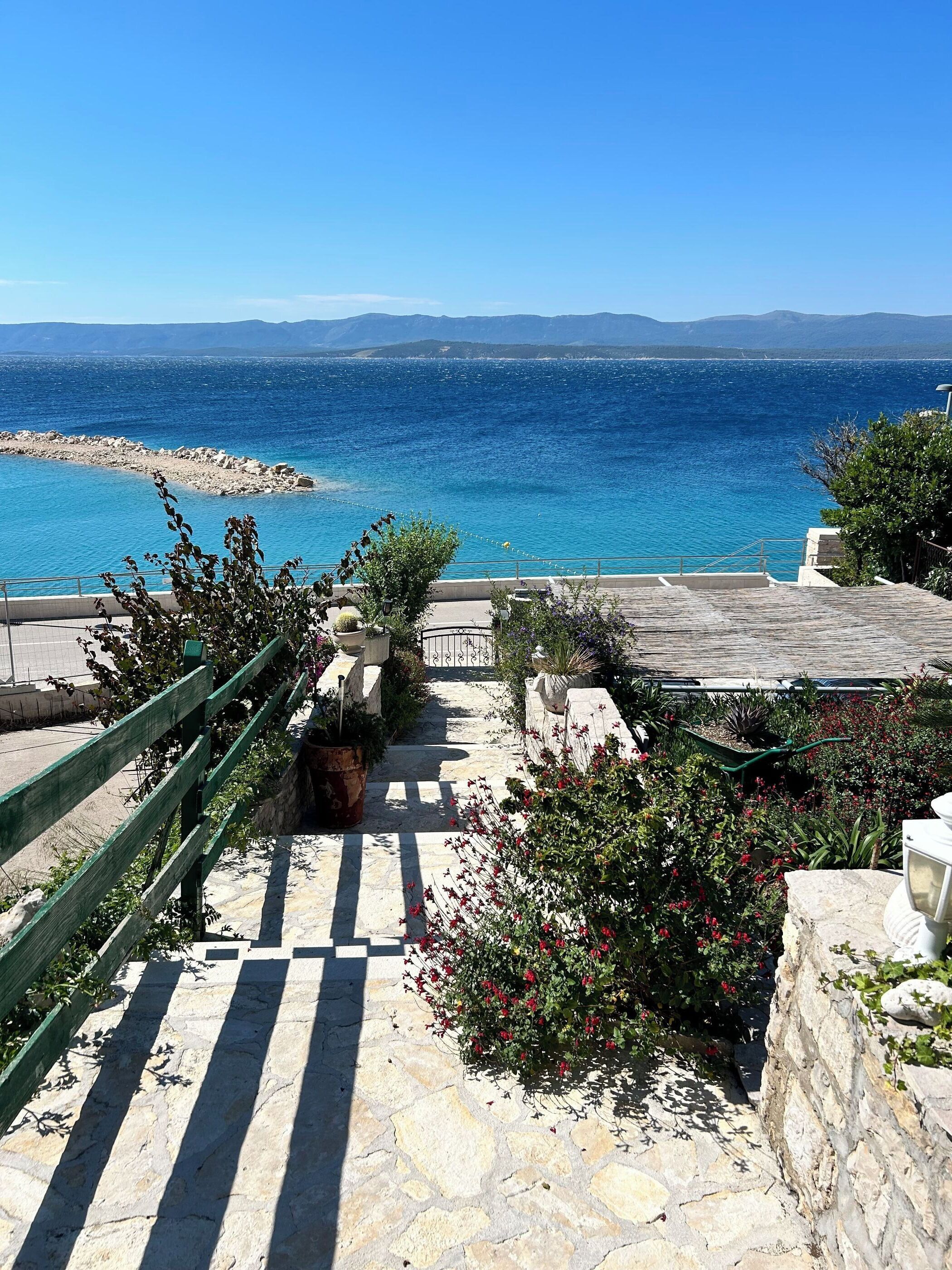 A stone staircase leading to a terrace overlooking a clear blue sea with distant mountains.