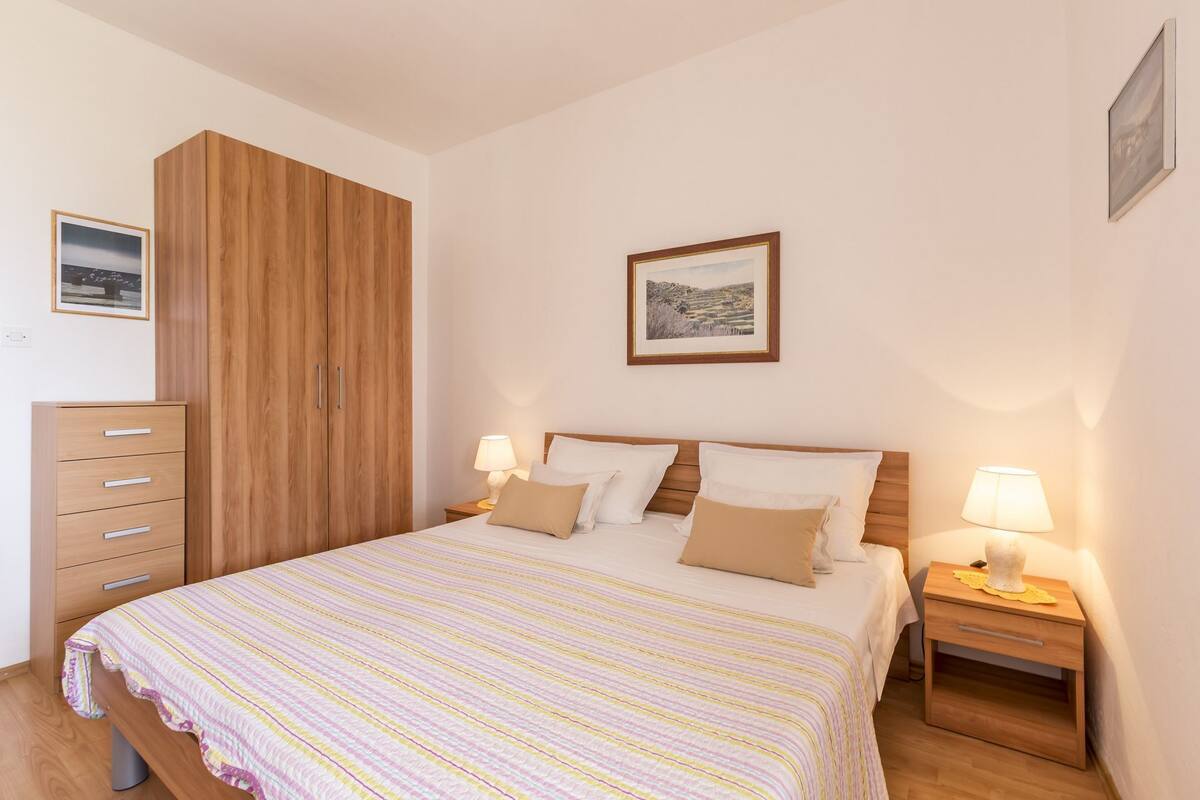 A bedroom with a bed, two bedside tables, a wardrobe, and two wall-mounted lamps.