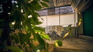 Un espacio al aire libre techado con una mesa y sillas, rodeado de vegetación.
