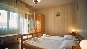 Una habitación con dos camas individuales, un armario de madera, una mesa con mantel de encaje y una ventana con cortinas traslúcidas.