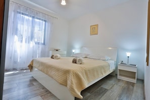 Ein ordentlich eingerichtetes Schlafzimmer mit Bett, Kissen, Nachttisch, Lampe und einem Fenster mit Vorhängen.