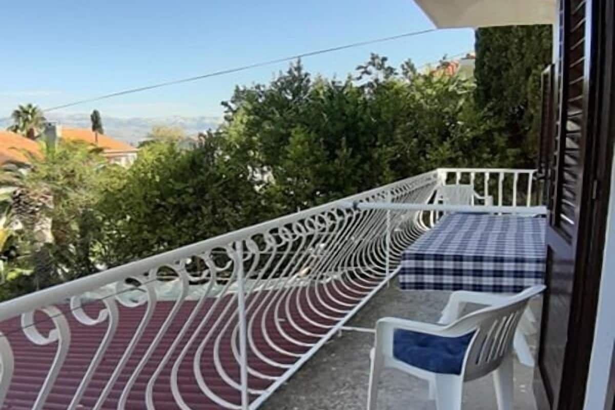 A balcony with a white railing, a small table with a checkered tablecloth, and a white plastic chair.