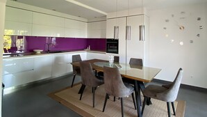 A modern kitchen with white cabinets, a purple backsplash, and a dining area with a glass table and chairs. - Apartments Nada (Sucuraj)