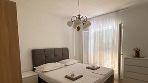 A modern bedroom with a large bed, bedside tables, a dresser, and a chandelier. - Apartments Nada (Sucuraj)