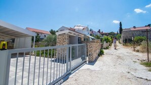 A residential area with houses, a paved driveway, and a stone wall. - Apartment Ivo (Supetar)