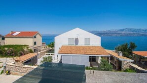 A coastal building with a white facade and a red-tiled roof, surrounded by other buildings and a clear view of the sea. - Apartment Ivo (Supetar)