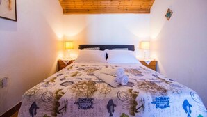 A bedroom with a wooden ceiling, a bed with a floral bedspread, two bedside lamps, and a framed picture on the wall. - Apartment Ivo (Supetar)