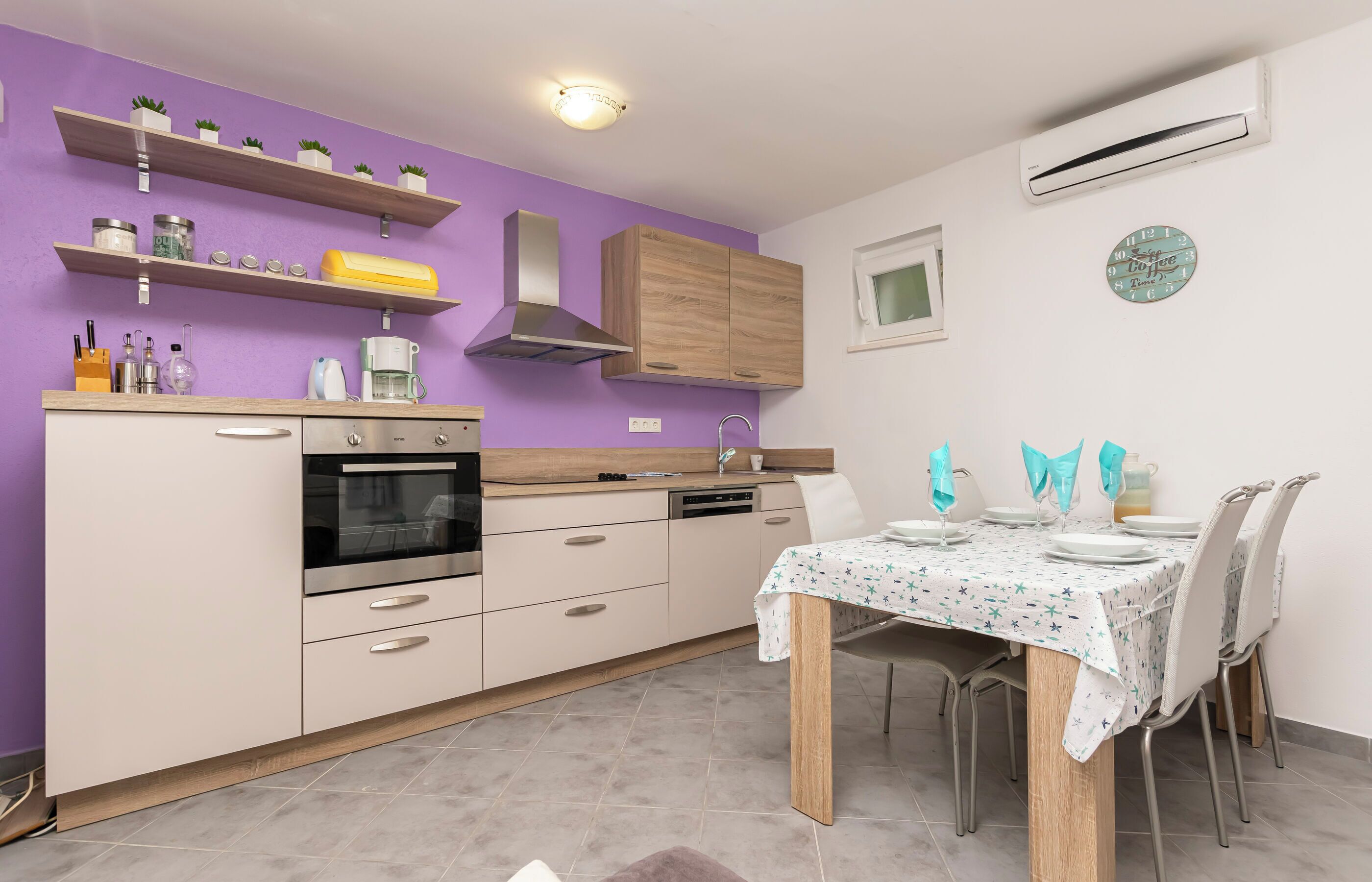 Une cuisine moderne dotée d’appareils électroménagers intégrés, de meubles de rangement en bois et d’un coin repas avec une table dressée pour quatre personnes.