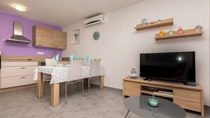 A modern kitchen with wooden cabinets, a dining table with chairs, a TV on a wooden stand, and a small table with a glass top. - Apartment Green (Dugi Rat)