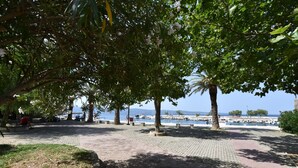 A paved walkway with benches and trees, leading to a waterfront with boats and a distant view of a cityscape. - Apartment Green (Dugi Rat)
