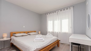 A bedroom with a wooden bed, white bedding, a bedside table with a lamp, a desk, and a chair. - Apartment Green (Dugi Rat)