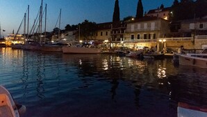 A marina at dusk with boats docked, buildings with balconies, and a calm water surface reflecting the lights. - Apartments Daira (Solta)