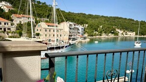 A balcony with a view of a marina, a table with a vase of flowers, and a railing. - Apartments Daira (Solta)