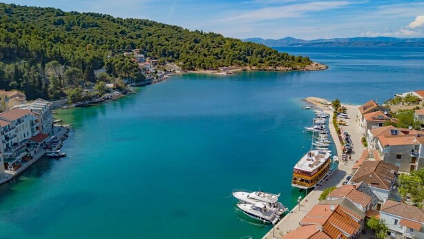 A coastal town with a marina, buildings with red-tiled roofs, and a hilly backdrop. - Apartments Daira (Solta)