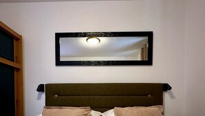 A neatly made bed with white linens and two beige pillows, a wooden headboard, and a mirror above it. - Apartments Daira (Solta)