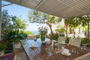 Un área de comedor al aire libre con una mesa preparada para dos personas, rodeada de plantas en macetas y vistas al mar.