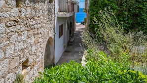 Une ruelle étroite, bordée de bâtiments aux murs de pierre, d’où l’on aperçoit la mer.