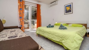 Une chambre avec un lit, un canapé, un balcon avec des rideaux orange et un appareil de climatisation.