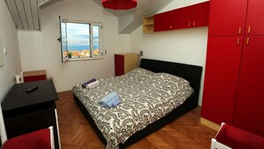 A bedroom with a bed, a desk, a chair, a red wardrobe, and a window with a view. - Apartment Aldica (Supetar)