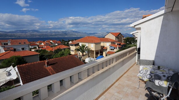 A balcony with a view of a coastal town, red-roofed buildings, and mountains in the distance. - Apartment Aldica (Supetar)