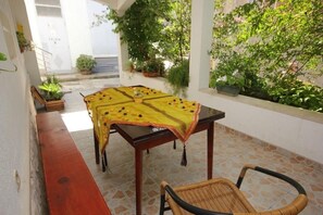 A covered outdoor seating area with a table and chairs, surrounded by potted plants and a view of a street. - Apartments Zoki (Vis)