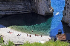 A beach with clear water, rocky cliffs, and people sunbathing. - Apartments Zoki (Vis)
