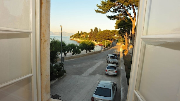 Vista desde una ventana con vista a una carretera costera, coches aparcados, árboles y cielo despejado.