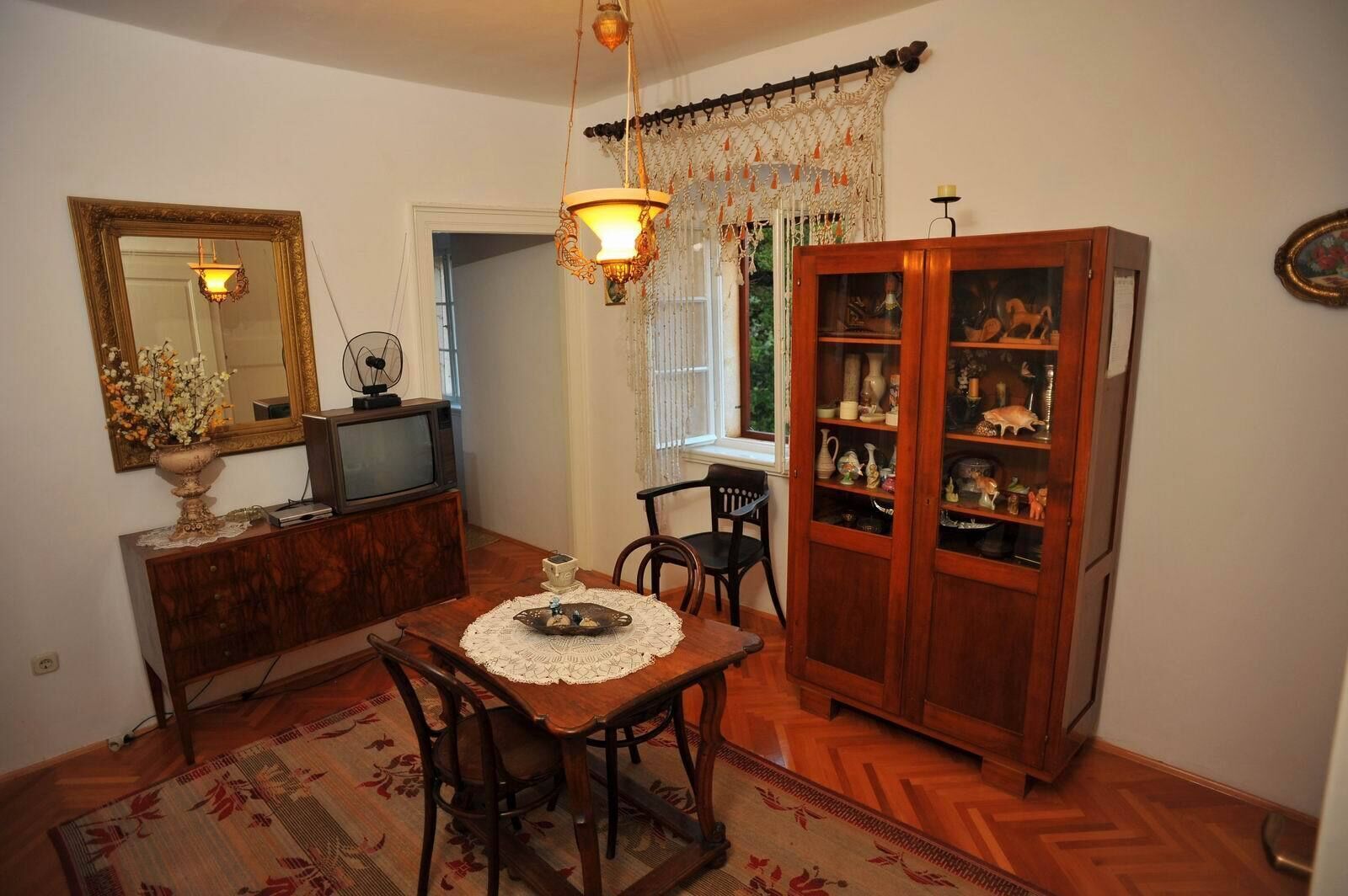 Un coin repas comprenant une table en bois, des chaises, un lustre, un téléviseur et un meuble contenant des objets décoratifs.