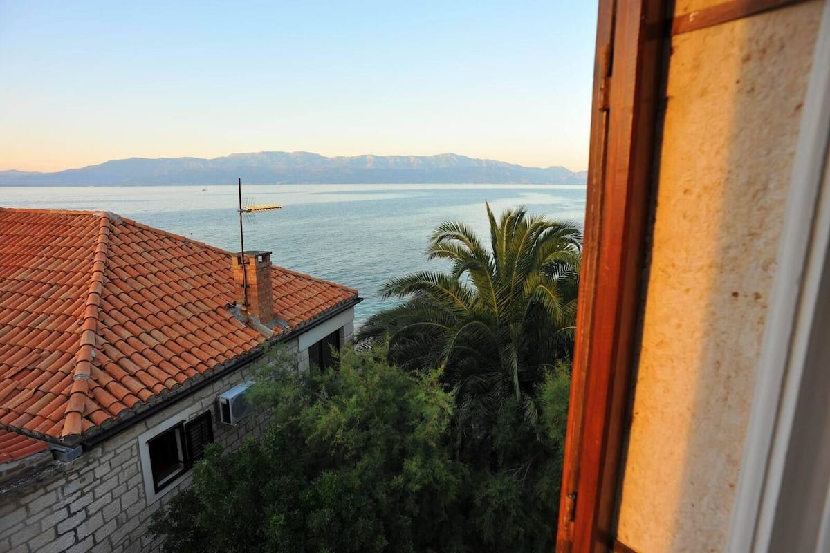 A coastal view with a tiled roof house, palm trees, and a distant mountain range.