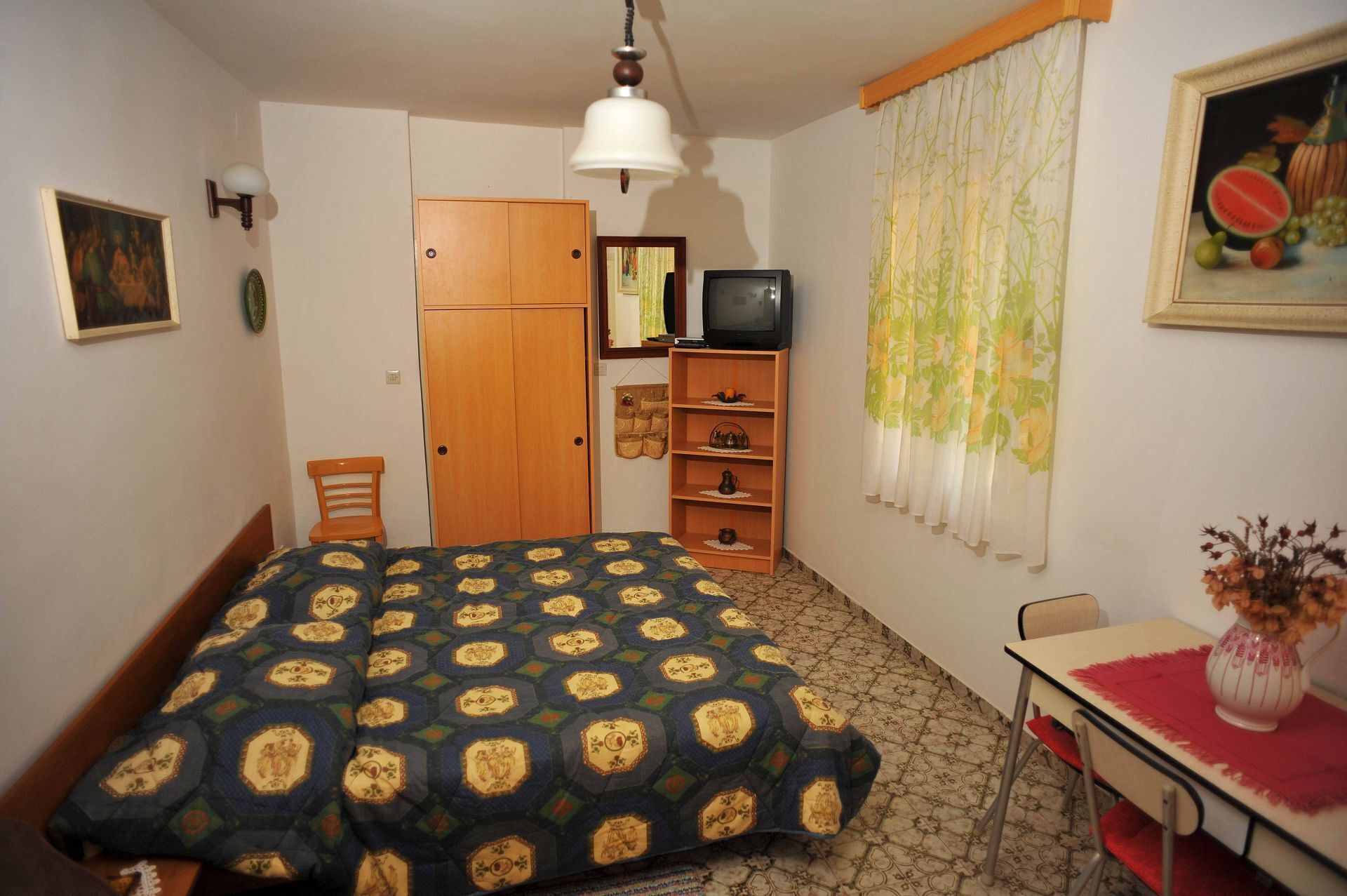 Ein Schlafzimmer mit Bett, Schreibtisch, Stuhl, Kleiderschrank, Fernseher und einem Bild an der Wand.