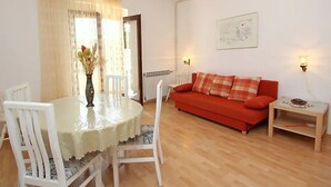 A living room with a round dining table, white chairs, a red sofa, and a small wooden side table. - Apartment Mari (Supetar)