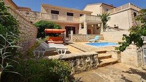 A courtyard with a swimming pool, stone walls, and outdoor seating. - Apartment Mari (Supetar)