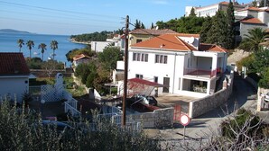 A coastal residential area with a prominent white building featuring a red-tiled roof, a balcony, and a stone wall. - Apartment Eta (Hvar)