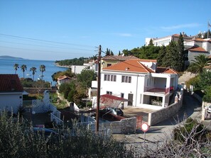 A coastal residential area with a prominent white building featuring a red-tiled roof, a balcony, and a stone wall. - Apartment Eta (Hvar)