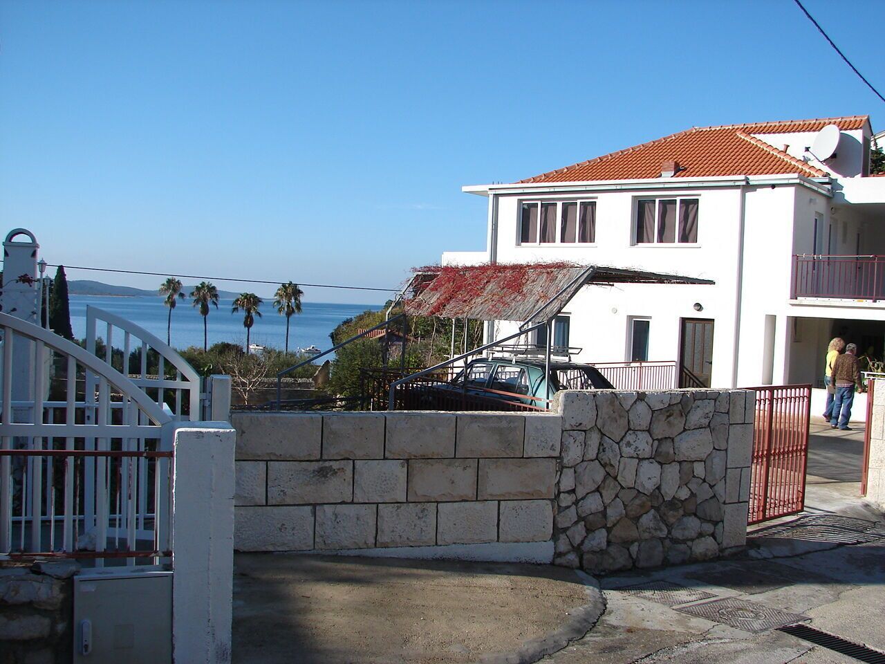 A coastal building with a red-tiled roof, a stone wall, and a white gate.