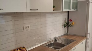 A kitchen with white cabinets, a wooden countertop, a stainless steel sink, and a refrigerator. - Apartments Marino (Supetar)